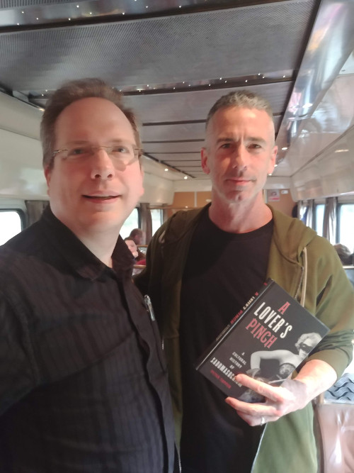 Peter Tupper standing next to Dan Savage, holding a copy of "A Lover's Pinch"